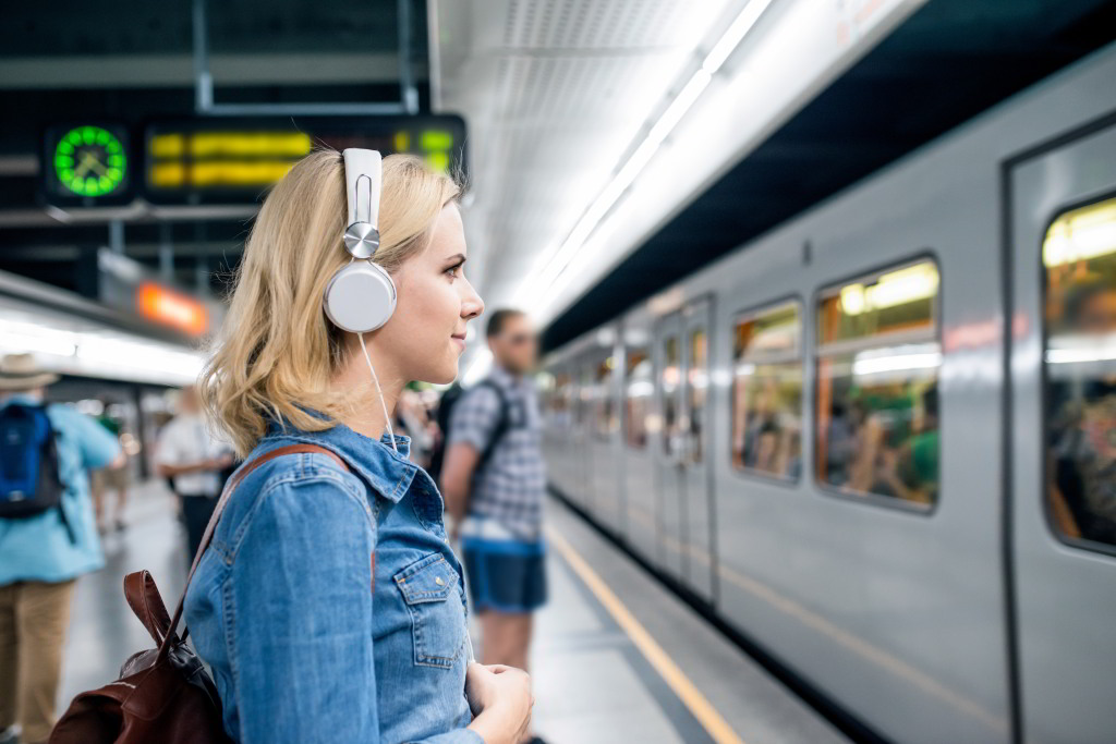 Eine junge Frau steht mit Kopfhörern am Bahnsteig, während die U-Bahn einfährt.