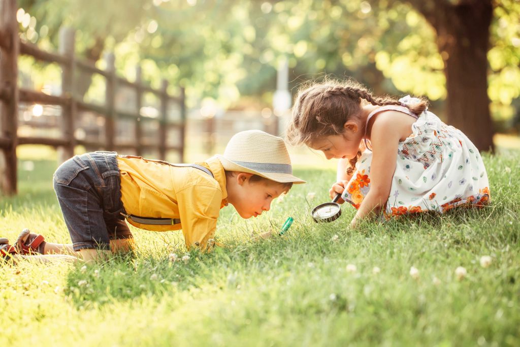 Zwei Kinder sitzen im Gras und schauen durch eine Lupe.