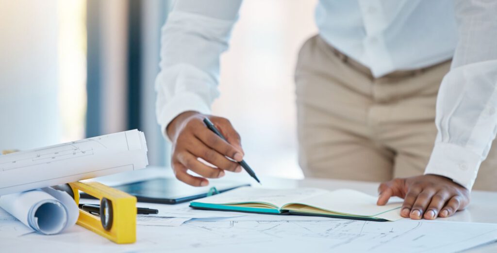 Headerbild zu Blogbeitrag mit Architekt, Schreiben und Planung mit einem Geschäftsmann Zeichnung in einem Notebook mit einer Blaupause und Plan auf einem Tisch in seinem Büro. Bau, Ingenieur und Architektur mit einem kreativen Entwurf bei der Arbeit.
