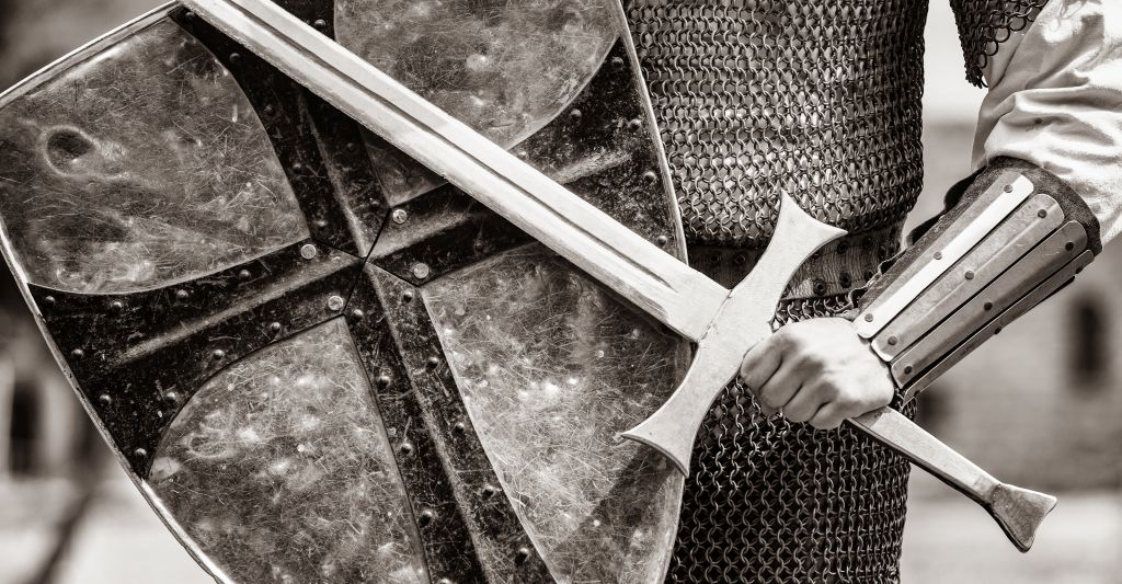 In Schwarz/Weiß: Ein Ritter hält ein Schild und Schwert vor sich in Verteidigung.