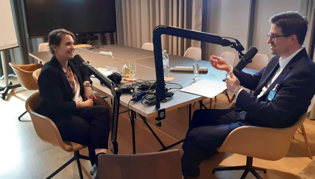 Zwei Personen, Iris Vonderhaid und Thomas Ziniel, die an einem Tisch sitzen, ausgestattet mit Mikrofonen und einem Laptop für die Aufzeichnung des Podcasts.