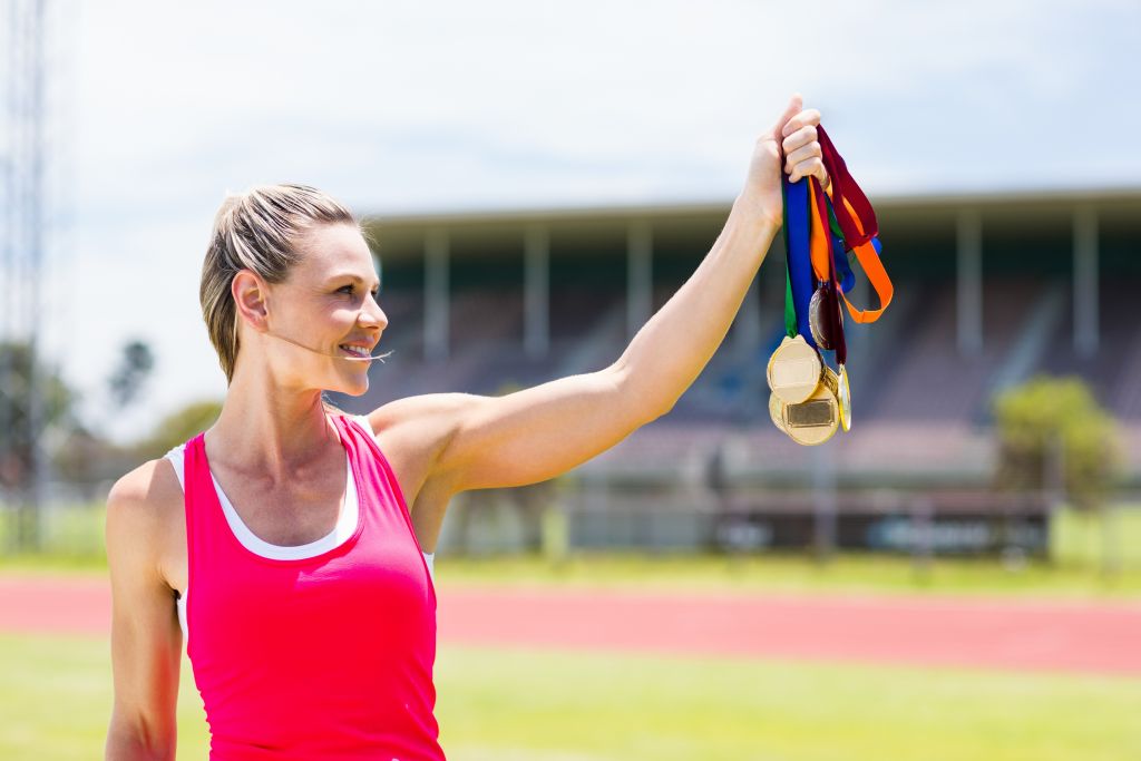 Eine Frau hält stolz ihre Goldmedaille auf der Rennstrecke. Sie strahlt vor Glück und Erfolg.